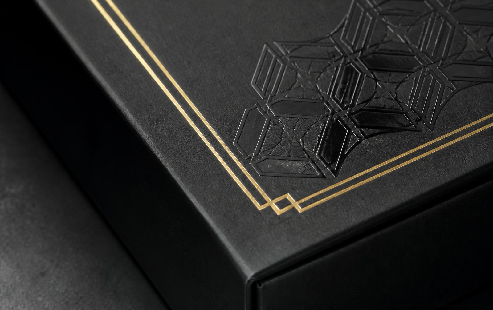 Macro detail of a matte black rigid box with gold foil line border and spot UV gloss pattern